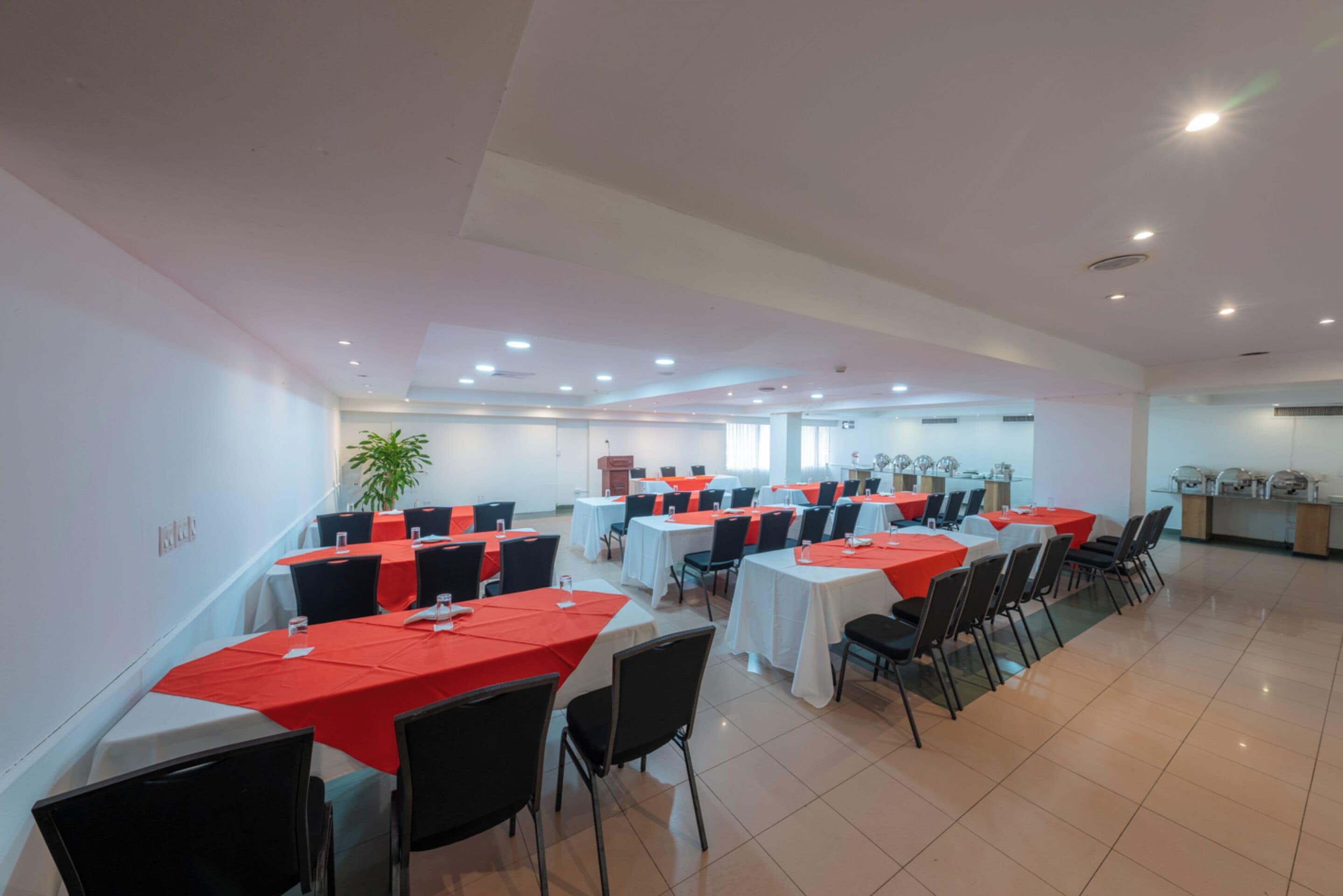 A conference room with multiple tables and chairs, white walls, and a tiled floor.