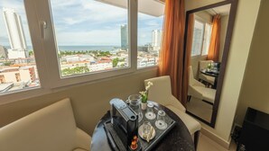 Habitación de hotel con un ventanal que ofrece vistas de la ciudad, una zona de comedor con una mesa preparada para dos personas y un espejo que refleja la habitación.