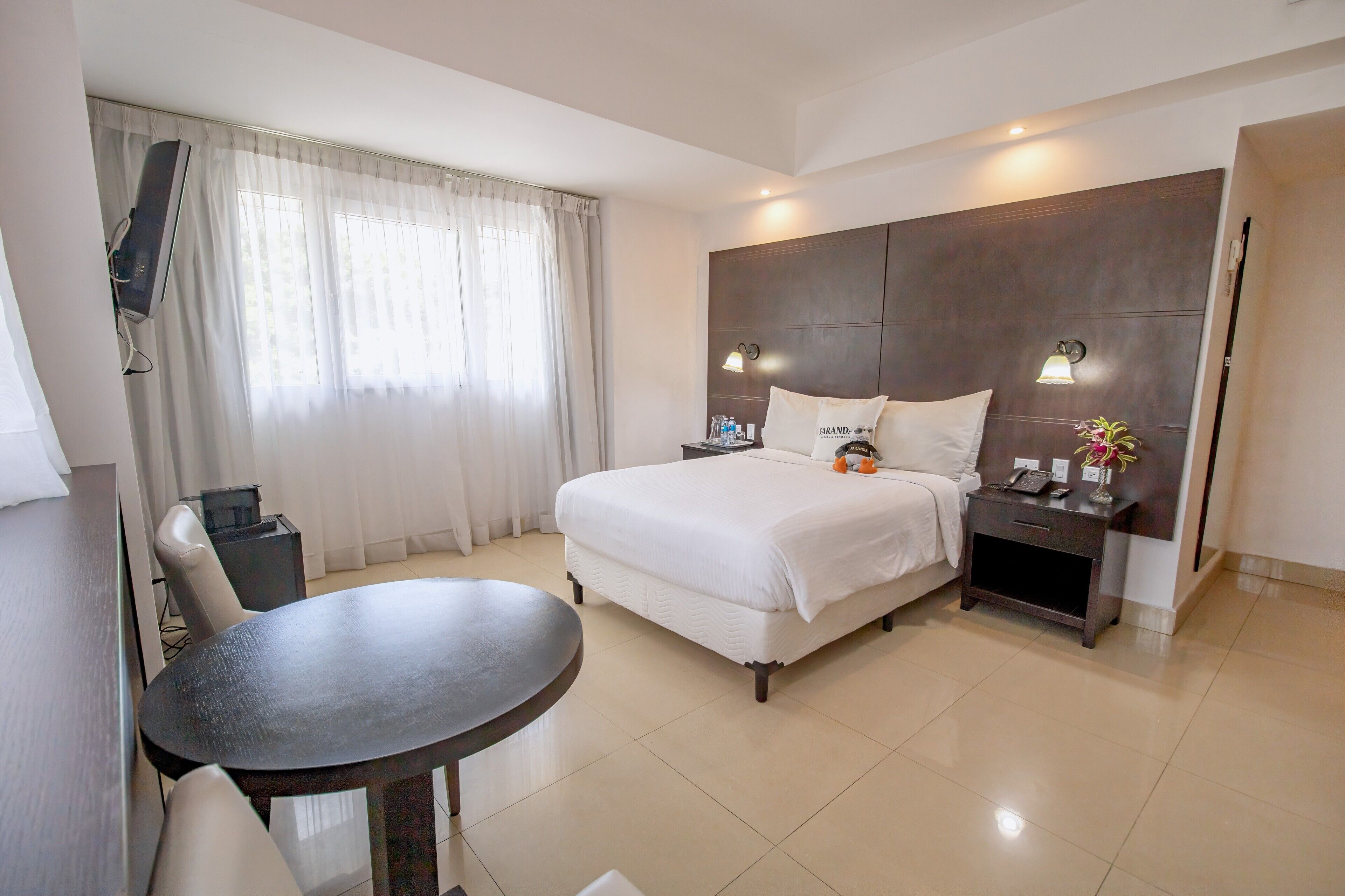 A hotel room with a bed, bedside table, lamp, and a TV mounted on the wall.