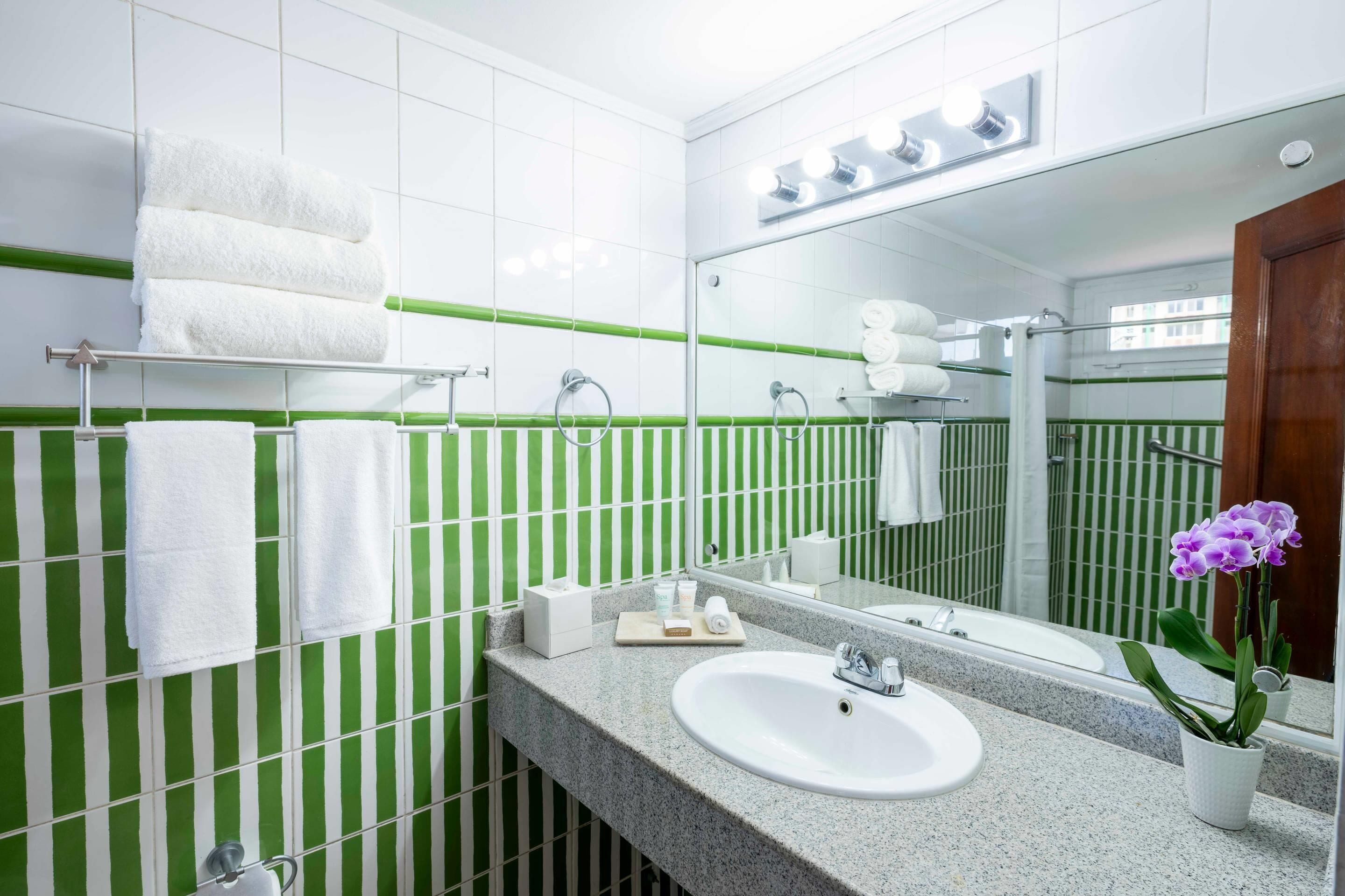 A bathroom with a white sink, green-striped tiles, and a mirror with lights above.