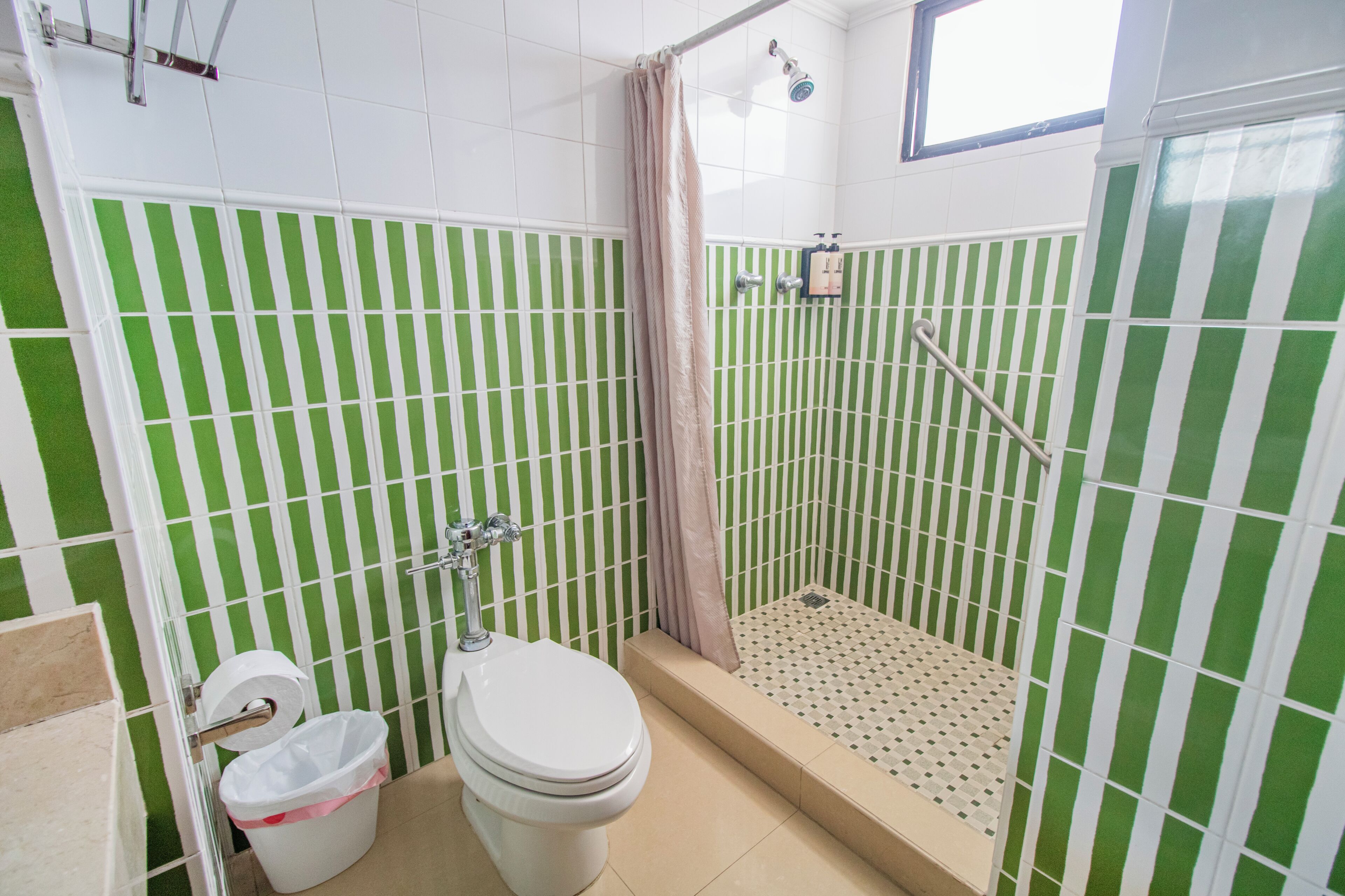 Un baño con inodoro, ducha y paredes verde rayadas.