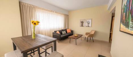 A modern living room with a dining area, a sofa, two armchairs, a coffee table, and a painting on the wall.
