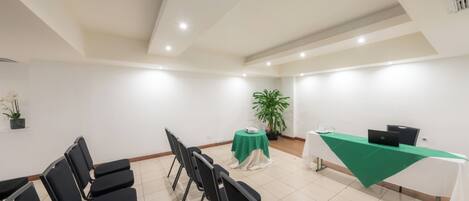 Un salón de conferencias con sillas negras, una mesa verde y un ordenador portátil sobre un mantel blanco.