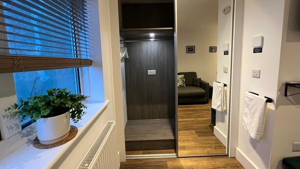 A narrow hallway with a sliding door leading to a room with a dark wooden door, a radiator, a plant, and a towel hanging on a rack. - Sea view, pet friendly central Laines location, 1 minute from station  (Brighton)
