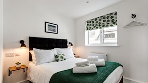 A neatly made bed with white linens and a green throw, a bedside table with a lamp, a framed picture on the wall, and a window with a leaf-patterned valance. - Sea view, pet friendly central Laines location, 1 minute from station  (Brighton)