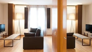A modern hotel room with a sofa, two tables, a TV, and two lamps. - MH Apartments Opera Rambla (Barcelona)