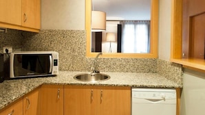 A compact kitchen with a granite countertop, a microwave, a sink, and wooden cabinets. - MH Apartments Opera Rambla (Barcelona)