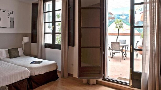 A hotel room with two beds, a large window, and an open door leading to an outdoor patio with a table and chairs. - MH Apartments Opera Rambla (Barcelona)