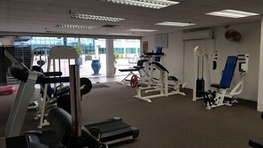 Un gimnasio con diversos equipos de ejercicio, una cinta de correr y un ventanal con vistas al exterior.