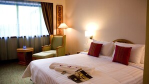 Habitación de hotel con una cama grande, una silla, una mesita de noche, una lámpara y un ventanal con cortinas.