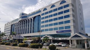 Un hotel moderno con varios pisos, amplias ventanas y un área de estacionamiento al frente.