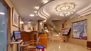 A hotel lobby with a reception desk, a computer monitor, a child play area, a staircase, and a large window with a view of the dining area. - Hispanos Siete Suiza (Barcelona)