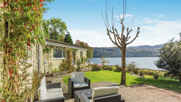 A patio with wicker furniture, a stone pathway, and a view of a lake and hills.