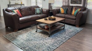 A living room with a brown leather sectional sofa, a wooden coffee table, a patterned rug, and a skylight.