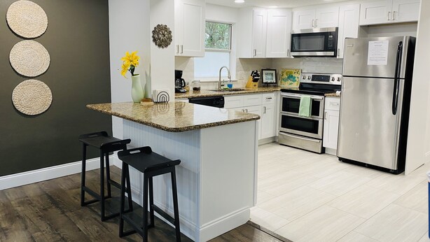A modern kitchen with white cabinets, stainless steel appliances, a granite countertop, and a wooden floor.