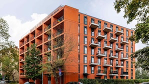 A multi-story orange building with balconies, a tree in front, and cars parked on the street.