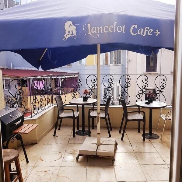 An outdoor cafe with a blue umbrella, metal chairs, and a small table with a grill. - Lancelot Hotel (Istanbul)