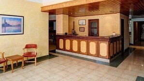 A reception area with a wooden reception desk, two red chairs, and a framed picture on the wall. - Estrella Hotel (Manacor)
