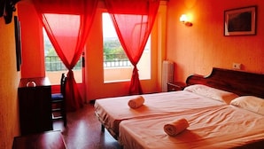A hotel room with two beds, a wooden nightstand, a small table, and a window with red curtains. - Estrella Hotel (Manacor)