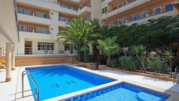 A swimming pool with a sun deck, surrounded by palm trees and a multi-story building with balconies. - Estrella Hotel (Manacor)