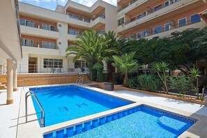 A swimming pool with a sun deck, surrounded by palm trees and a multi-story building with balconies. - Estrella Hotel (Manacor)