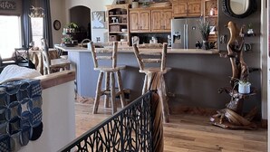 A spacious kitchen with wooden cabinets, a dining area with a high wooden table, and a staircase leading to an upper level. - Mountain View Spacious Ranch Home AMAZING VIEW (Milliken)