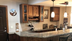 A kitchen with wooden cabinets, a bar area with stools, and a wine rack. - Mountain View Spacious Ranch Home AMAZING VIEW (Milliken)