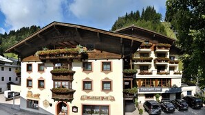 Ein traditionelles Gebäude im alpinen Stil mit mehreren Balkonen, die mit Blumenkästen geschmückt sind, einem Schild mit der Aufschrift "Gathof Post" und mehreren parkenden Autos davor.