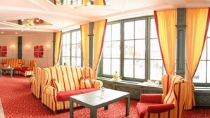 Eine Hotelhalle mit gestreiften Sesseln, einer Couch, einem Tisch und großen Fenstern mit Vorhängen.