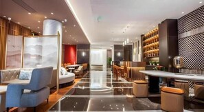 Un hall d’hôtel moderne, doté d’espaces aménagés avec des sièges, d’un bar et d’un comptoir de réception.