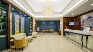 A hotel lobby with a reception desk, seating area, and a chandelier.