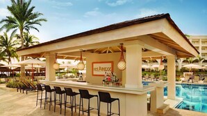 A bar area with a poolside view, featuring a bar counter, black bar stools, and umbrellas. - Hyatt Zilara Rose Hall - Adults Only (Montego Bay)