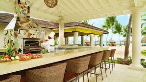 An outdoor bar area with a mosaic-tiled bar counter, wicker bar stools, and a pizza oven. - Hyatt Zilara Rose Hall - Adults Only (Montego Bay)