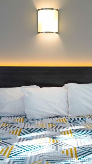 A hotel room with a bed, a headboard, and a wall-mounted light fixture.