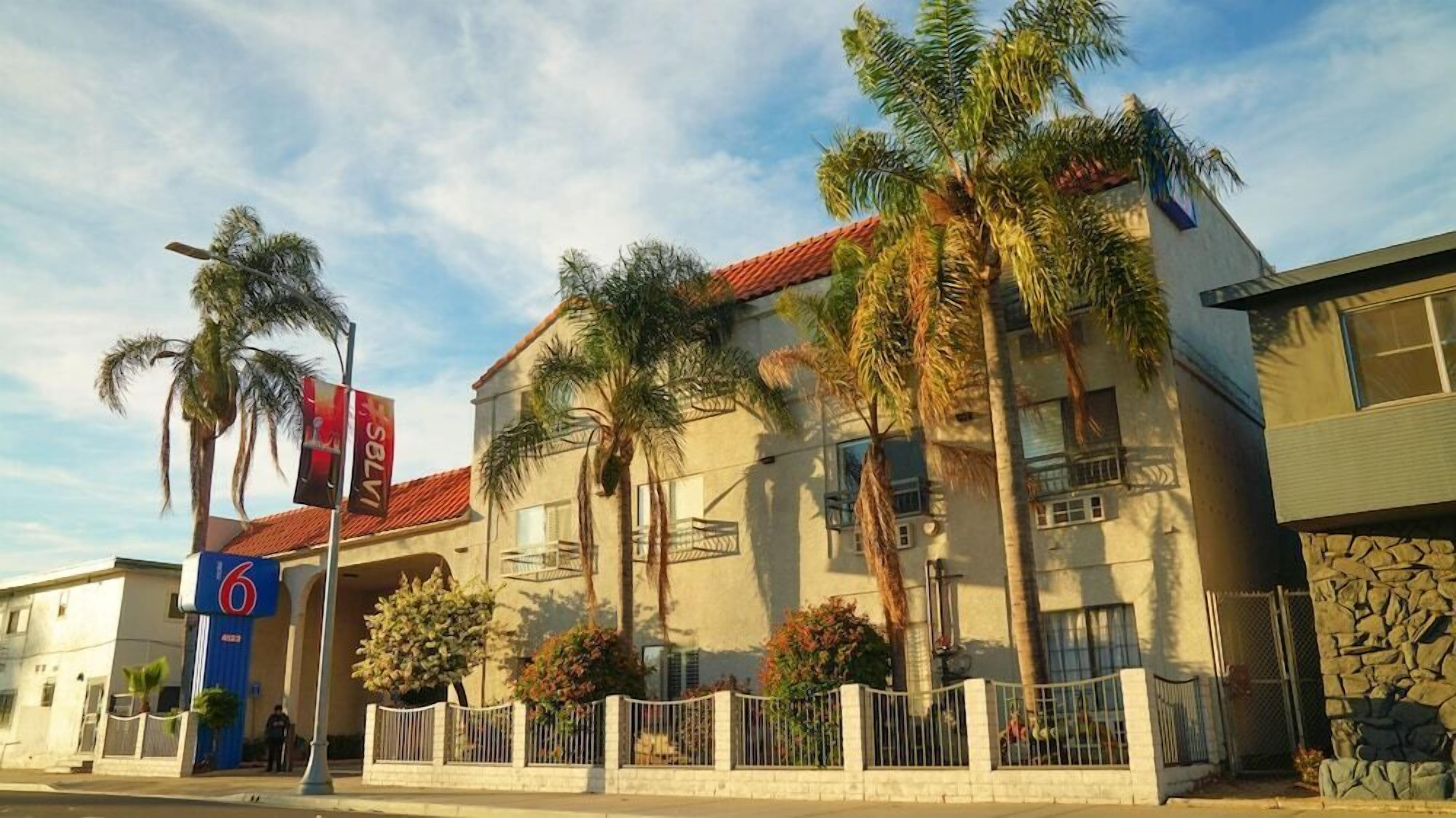 A hotel with a red-tiled roof, palm trees, and a stone facade.