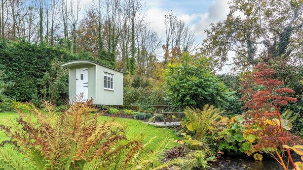 A small, light-colored shed in a lush garden with a stream and various plants. - 1 bedroom accommodation in Thirlby, near Thirsk (Thirlby, near Thirsk)