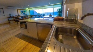 Une cuisine moderne dotée d’un grand îlot central, d’un évier en acier inoxydable et offrant une vue sur l’extérieur grâce à de grandes fenêtres.