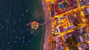 Vue aérienne d’une zone côtière avec une promenade illuminée, une plage et plusieurs bateaux.