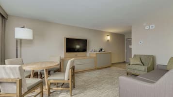 Habitación de hotel con mesa de comedor, sillas, sofá, televisor y minibar.