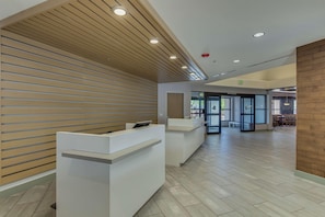 A reception area with a wooden slat wall, white reception desks, and a tiled floor. - Doubletree by Hilton Phoenix Chandler (Chandler)