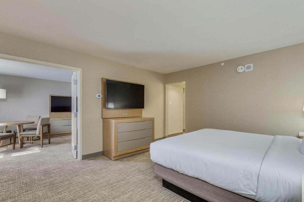 A hotel room with a bed, a TV, a desk with chairs, and a dresser.