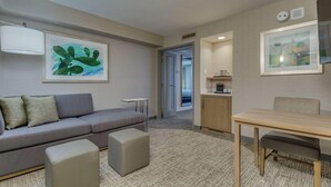 A modern hotel room with a grey sofa, a small table, a cabinet, and artwork on the walls.