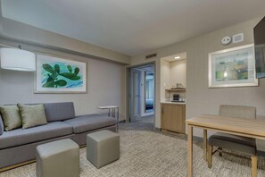 A modern hotel room with a grey sofa, a small table, a cabinet, and artwork on the walls. - Doubletree by Hilton Phoenix Chandler (Chandler)