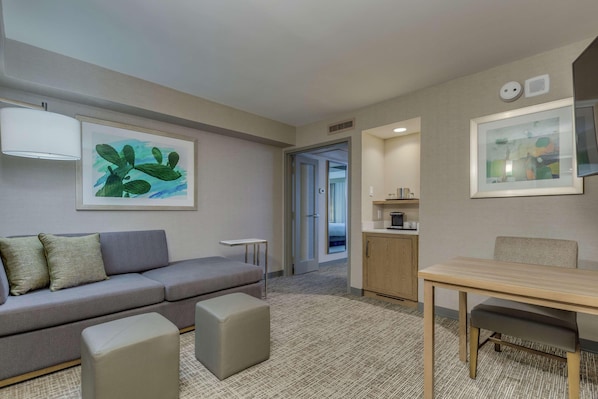 A modern hotel room with a grey sofa, a small table, a cabinet, and artwork on the walls. - Doubletree by Hilton Phoenix Chandler (Chandler)