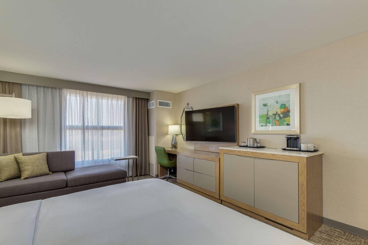 A hotel room with a bed, a sofa, a TV, a desk, and a painting on the wall.