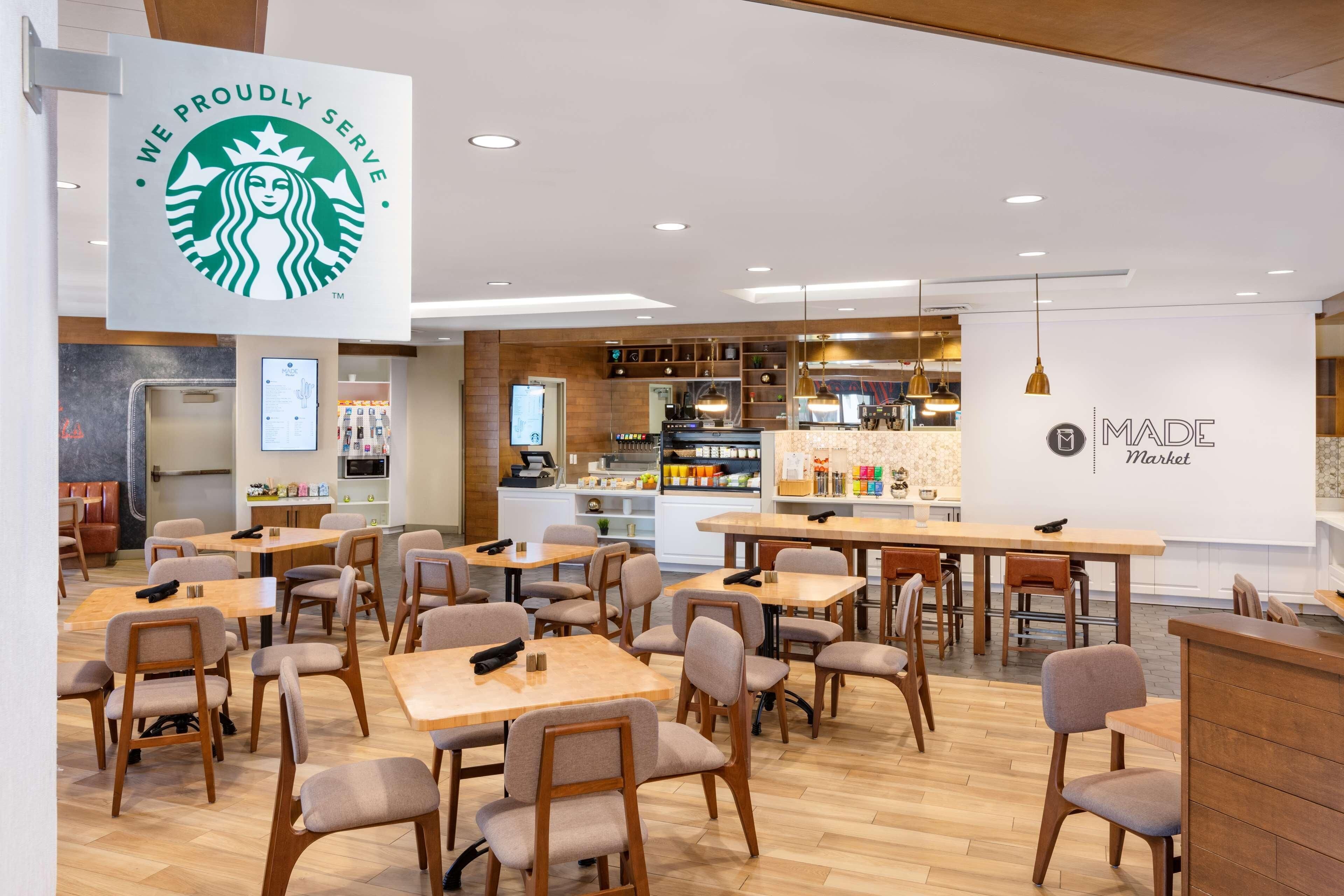Una cafetería Starbucks con mesas y sillas, una máquina de café y una pared con el logotipo de Starbucks.