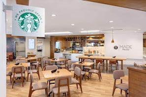 Un café Starbucks avec des tables et des chaises, une machine à café et un mur orné du logo de Starbucks.