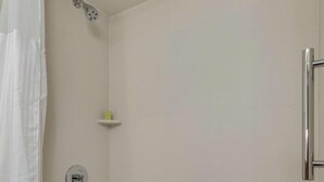 A bathroom with a bathtub, a showerhead, a towel, and a shelf.