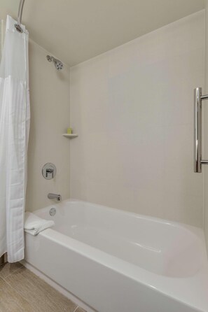 A bathroom with a bathtub, a showerhead, a towel, and a shelf. - Doubletree by Hilton Phoenix Chandler (Chandler)