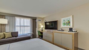 A hotel room with a bed, a sofa, a TV, a desk, and a painting on the wall.